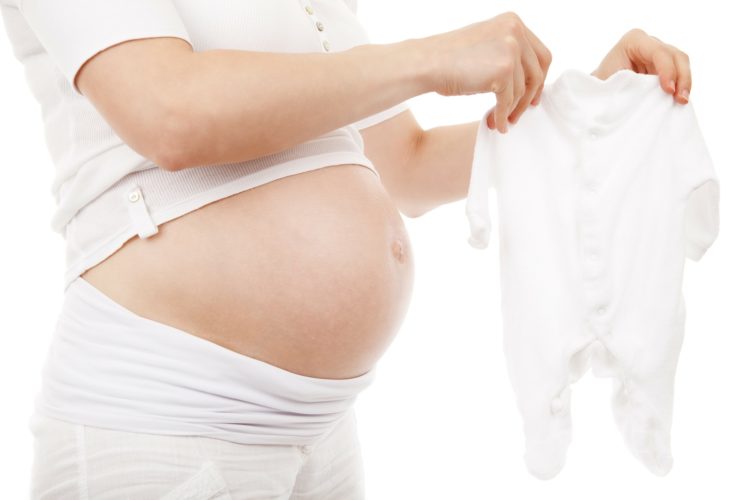 赤ちゃんの洋服を持っている妊娠中の女性